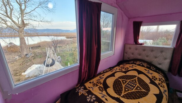 A bedroom with a large window, a view of a rural landscape, and a tufted headboard.