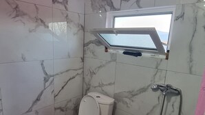 A bathroom with a toilet, a shower, and a window.