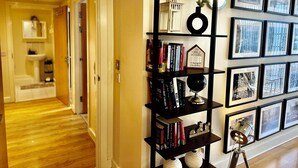 A hallway with a wooden floor, a black bookshelf with books and decorative items, and a wall with framed pictures. - Urban Chic: 2BR + FREE Parking (Birmingham)