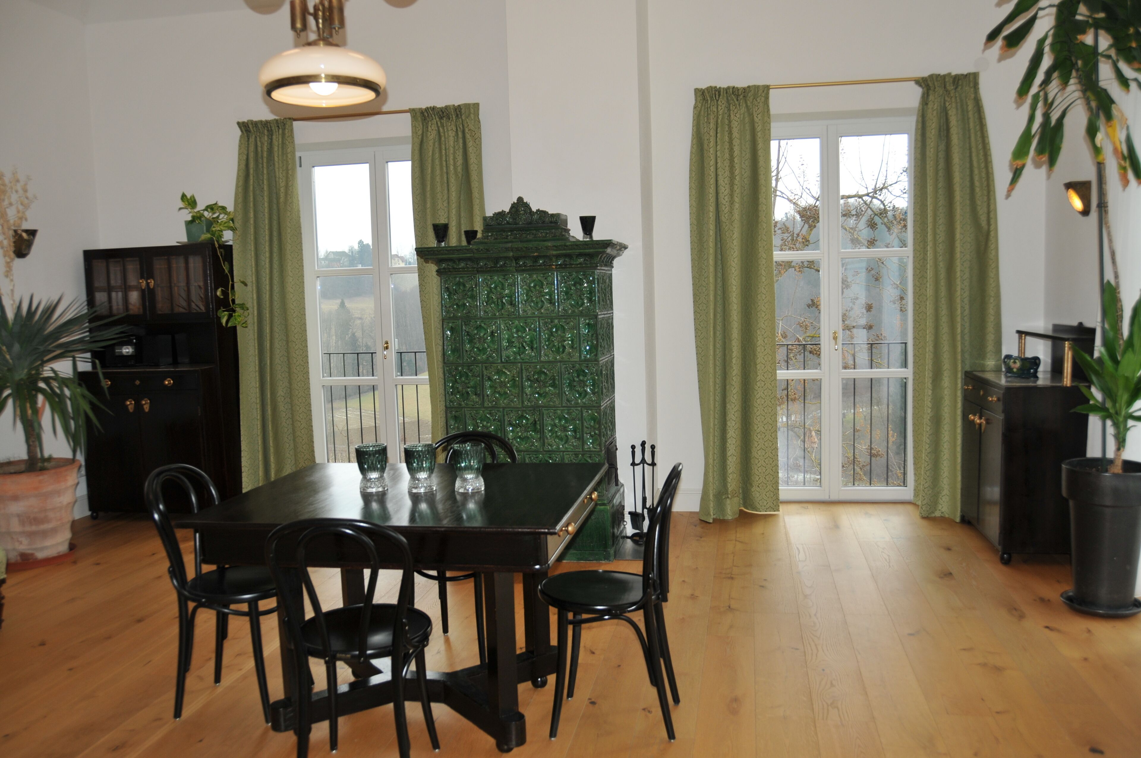 Een eetkamer met een houten tafel en stoelen, een groen kastje en een raam met gordijnen.