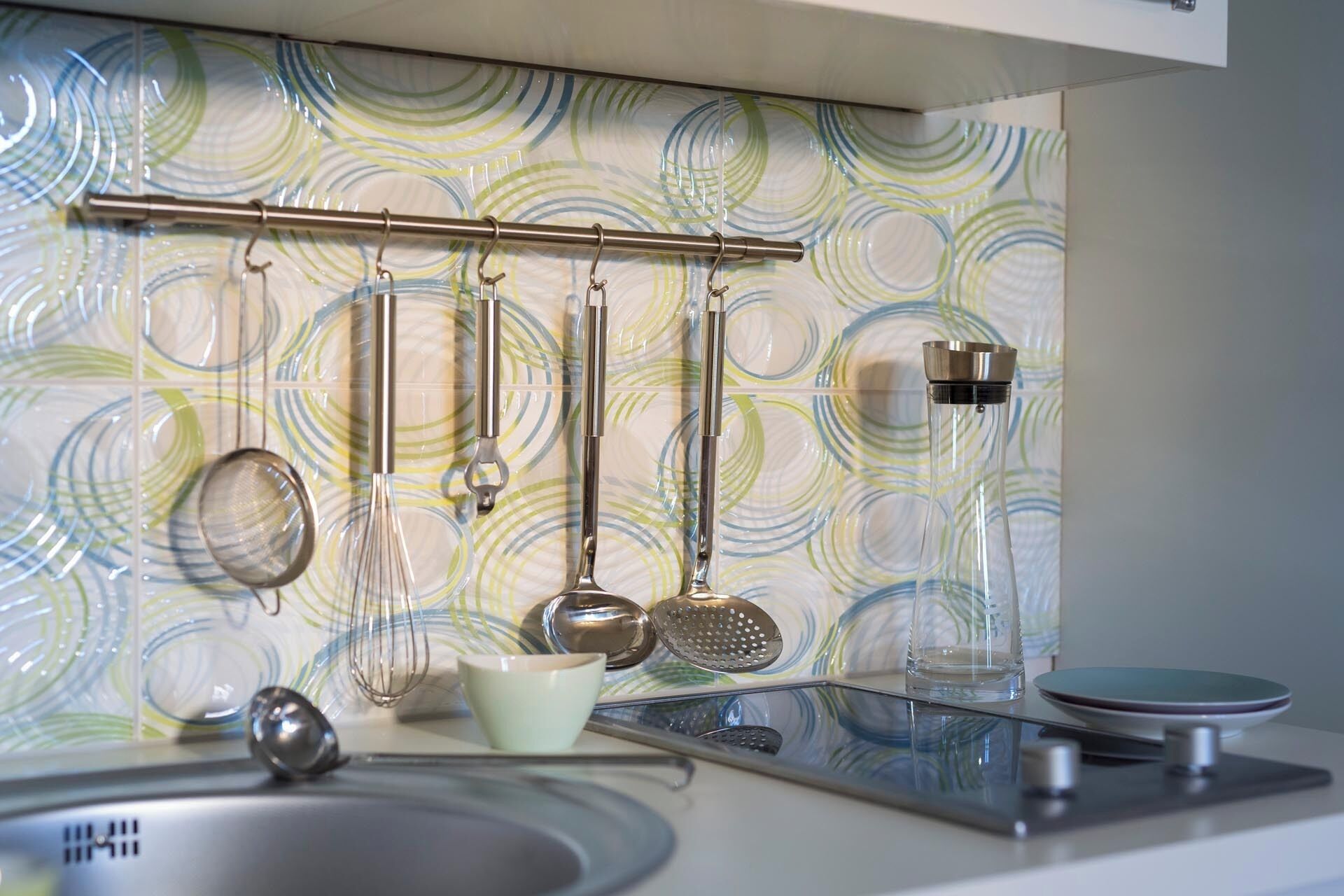 A kitchen with a modern backsplash, a stainless steel sink, and various utensils hanging above it.