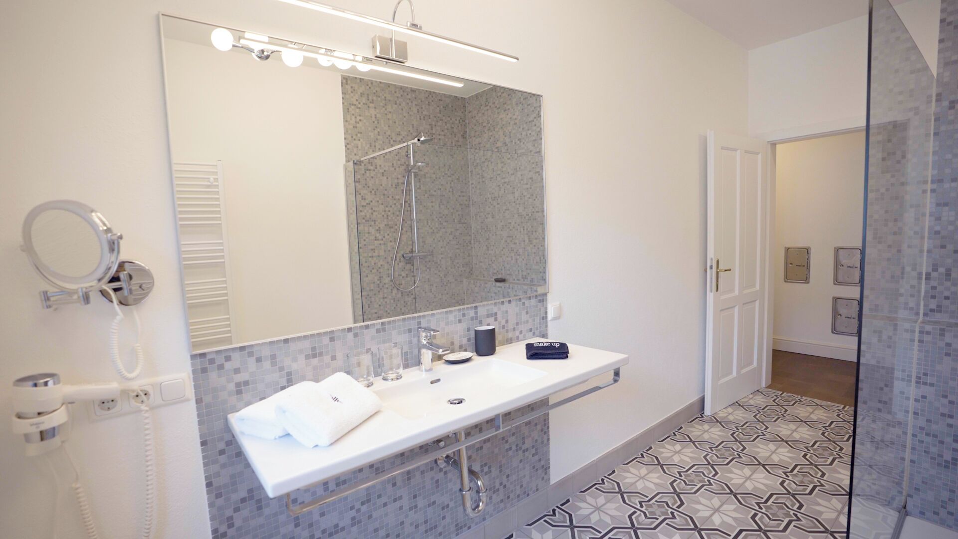 A modern bathroom with a large mirror, a vanity with a sink, a handheld showerhead, and a towel rack.