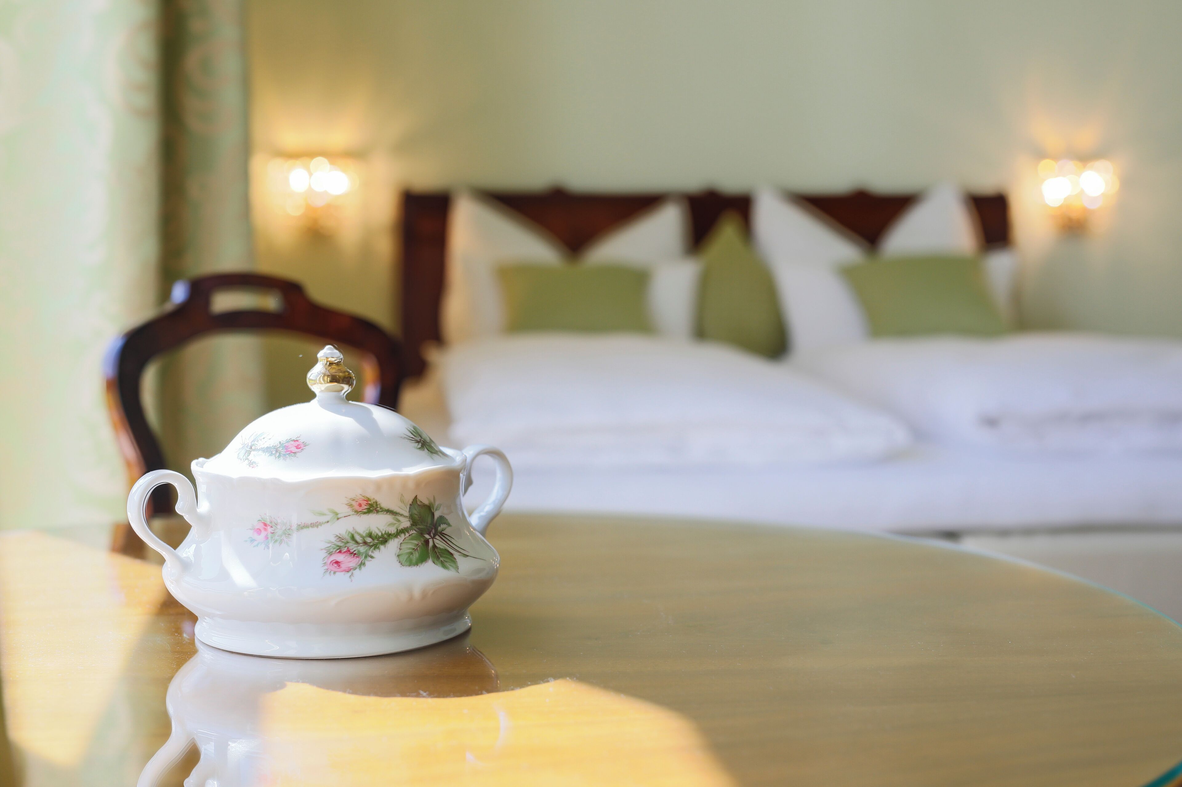 A white teapot with floral designs on a wooden table in a hotel room.