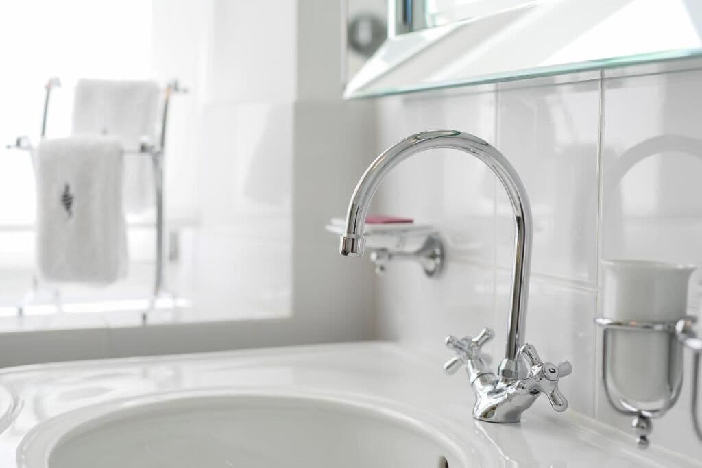 A modern bathroom with a glass shelf, a chrome faucet, and a white sink.