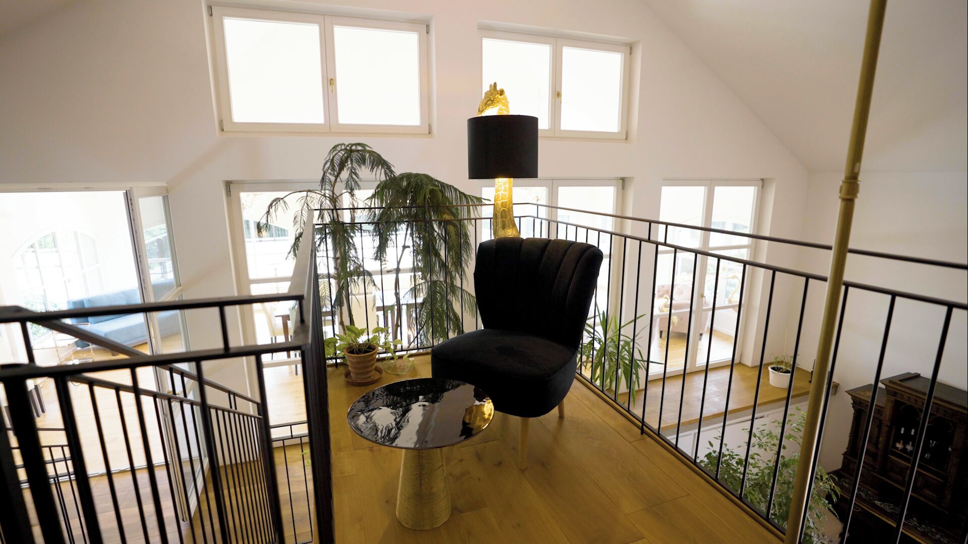 A spacious loft with high ceilings, large windows, a black armchair, a glass coffee table, and a giraffe sculpture.