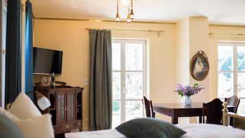A bedroom with a bed, a TV, a wooden cabinet, a table with a vase, and a window with curtains.
