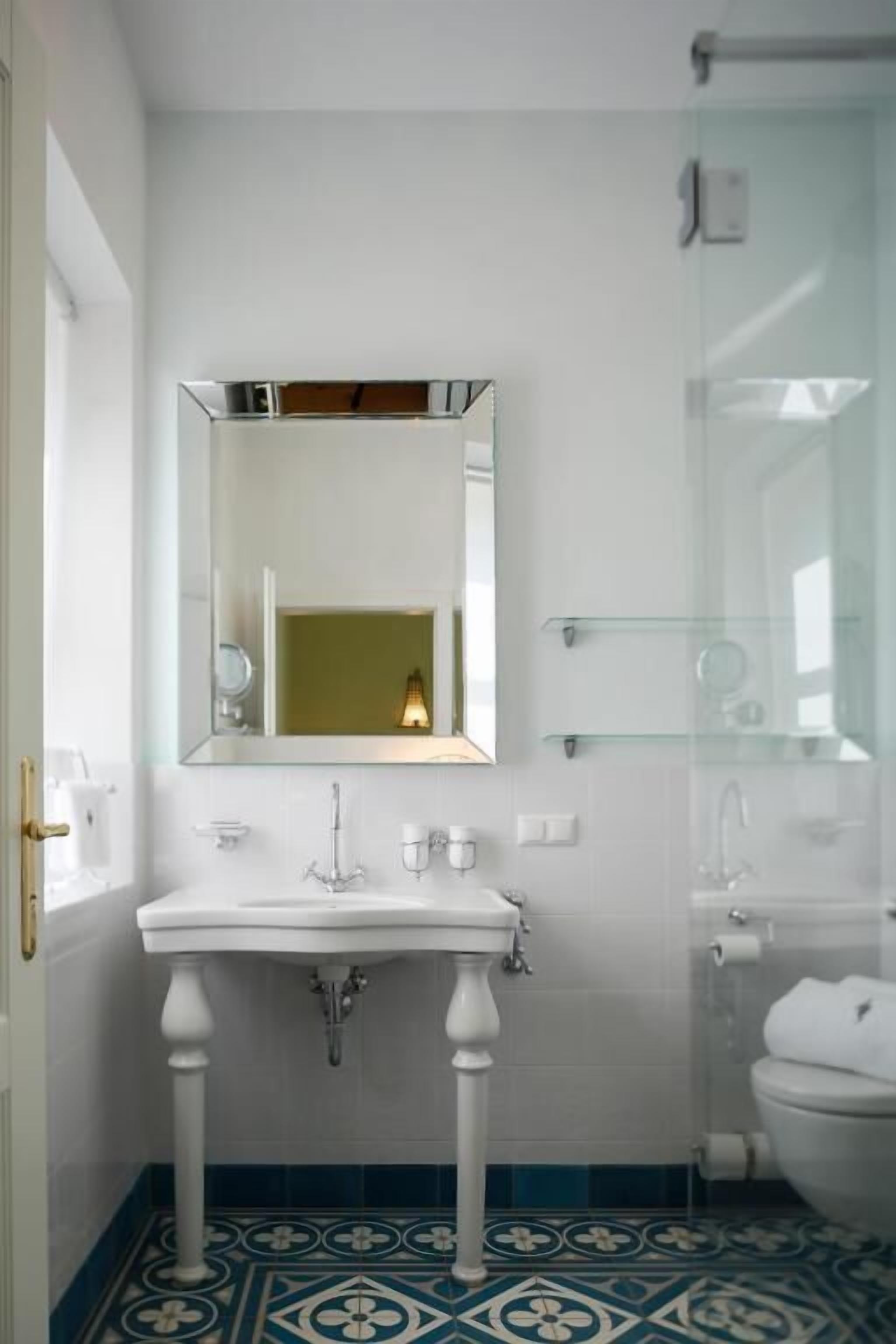 A bathroom with a white pedestal sink, a mirror above it, and a toilet.