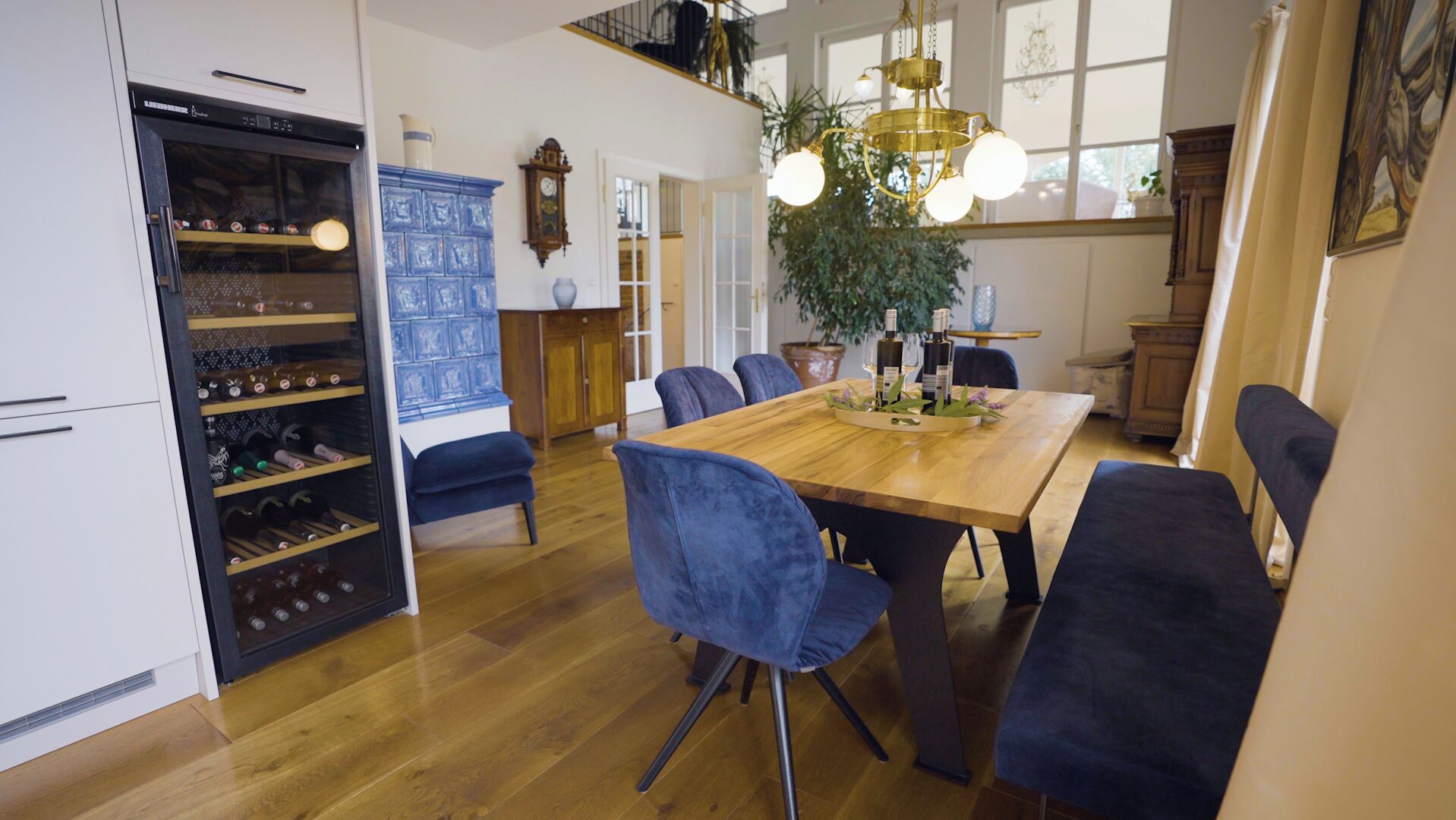 A spacious dining area with a wooden table, blue upholstered chairs, and a chandelier.