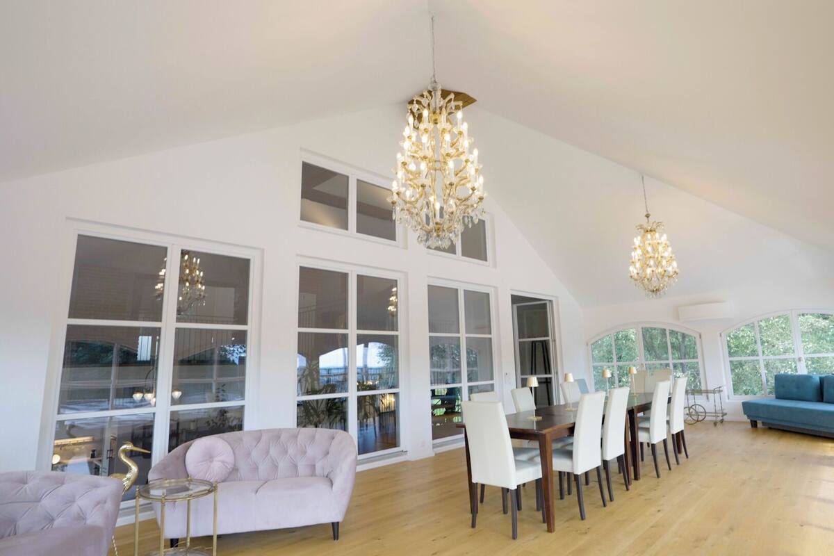 A spacious room with high ceilings, large windows, and a dining area with a table and chairs.
