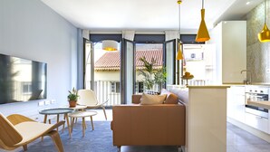 A modern living room with a sofa, chairs, a small table, and a kitchen area with a counter and cabinets. - Solaga - Alta (Málaga)