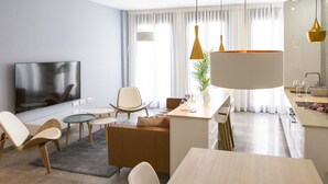 A modern living room with a flat-screen TV, seating area, and a kitchen with a bar. - Solaga - Alta (Málaga)