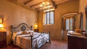 A bedroom with a bed, wooden headboard, two bedside tables with lamps, a dresser, a mirror, and a window with curtains.