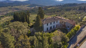 A two-story house with a tiled roof, surrounded by trees and hills.