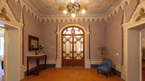 A spacious room with a large wooden door, a blue armchair, and a small table with a vase.