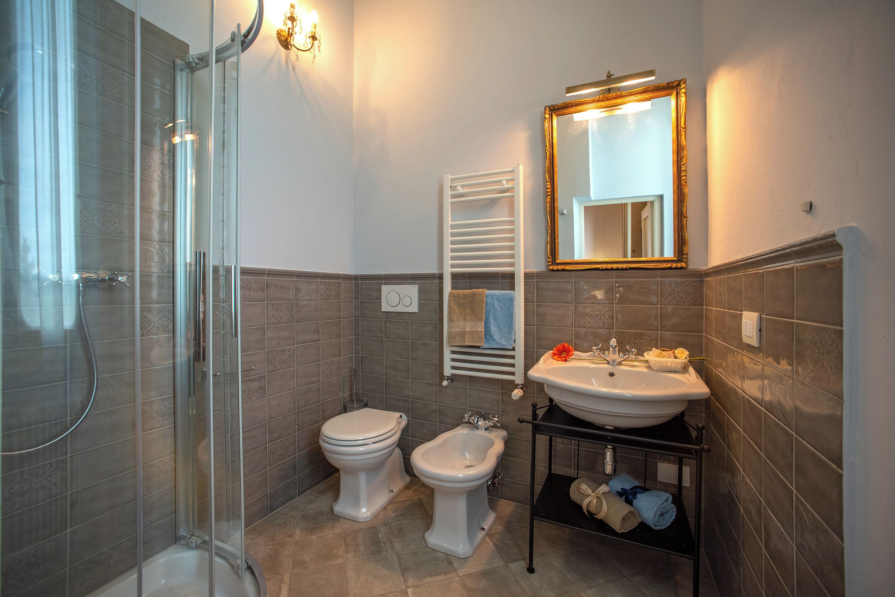 A bathroom with a glass shower enclosure, a toilet, a bidet, and a sink with a mirror above it.