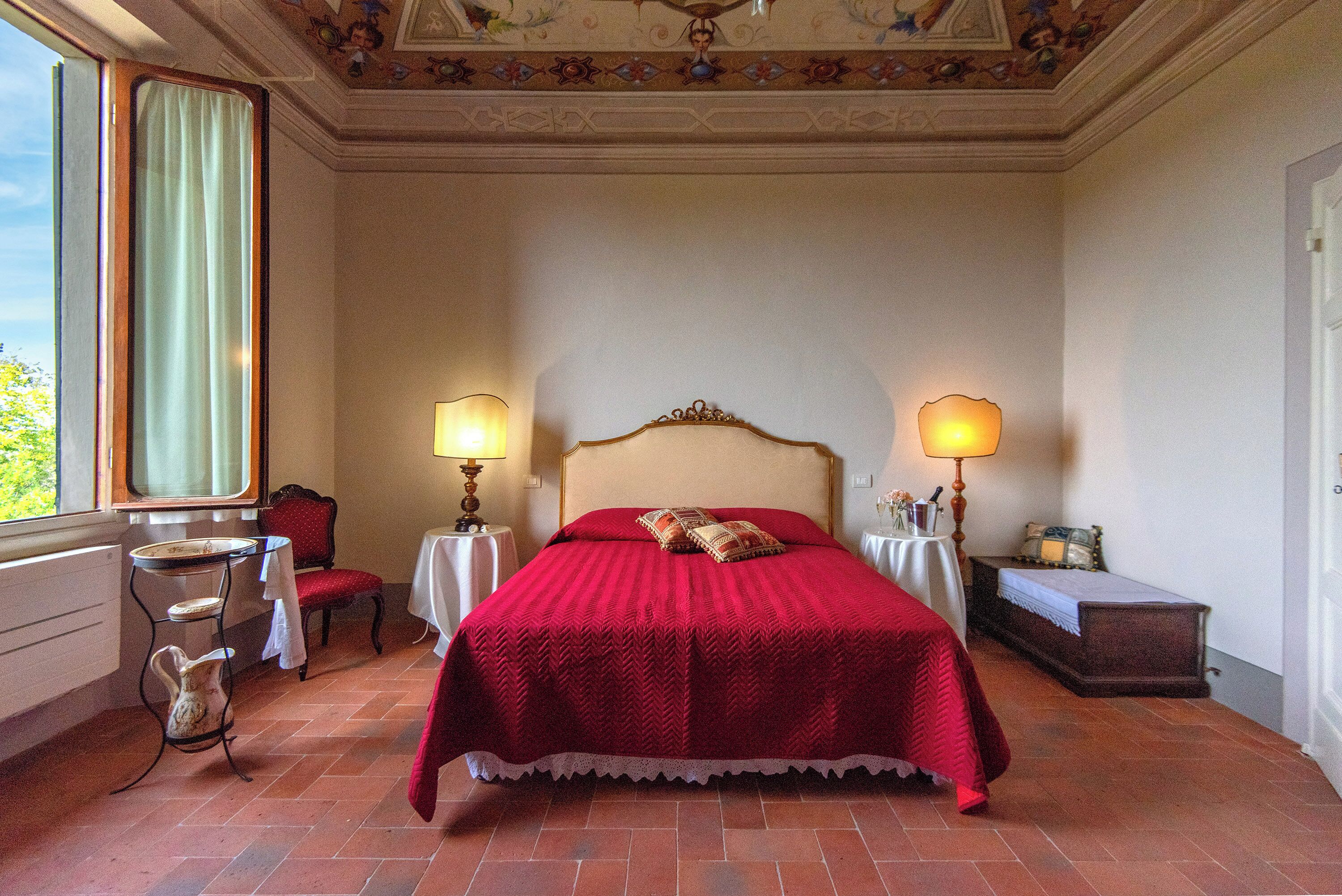 A bedroom with a large bed, two bedside tables with lamps, a chair, and a small table with a vase.