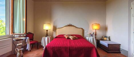 A bedroom with a large bed, two bedside tables with lamps, a chair, and a small table with a vase.
