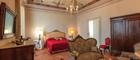 Quarto com uma cama, duas poltronas, um armário de madeira e um candelabro.