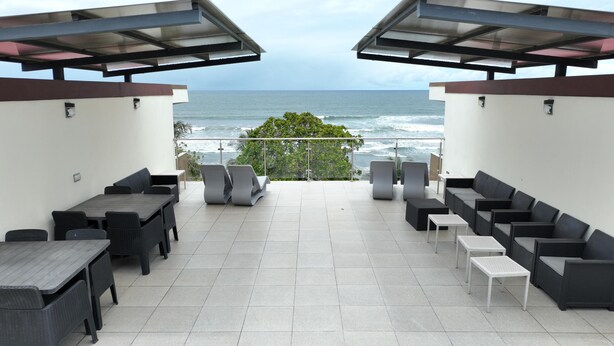 A terrace with a view of the ocean, furnished with tables and chairs, and a glass railing. - Stylish Oceanfront Condo 3205 | Playa Bejuco + Bright Design + Pool (Bejuco)