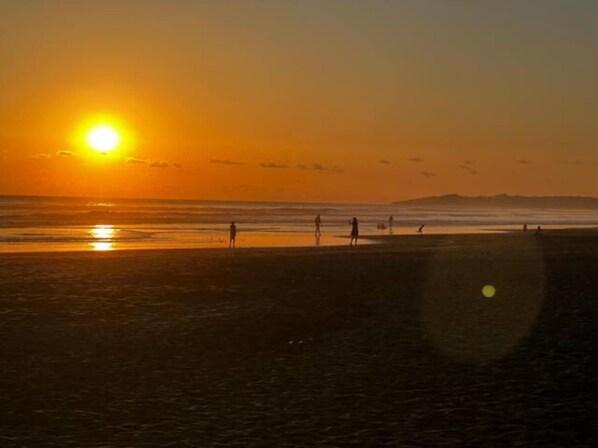 Una playa al atardecer, con gente caminando por la orilla.