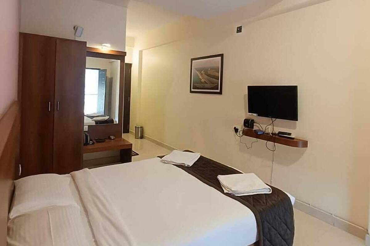 Hotellihuone, jossa on sänky, puinen vaatekaappi, jalustalla oleva televisio ja kattotuuletin.