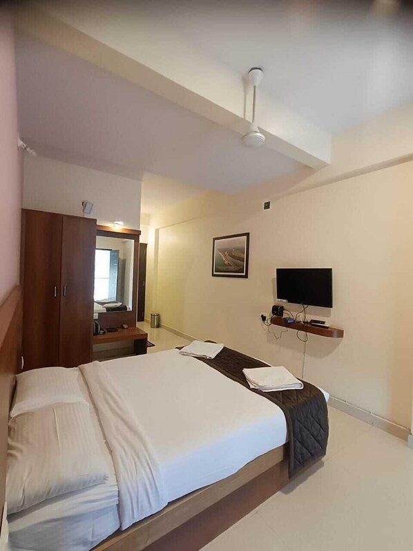 Une chambre d’hôtel avec un lit, une armoire en bois, un téléviseur posé sur un meuble et un ventilateur de plafond.