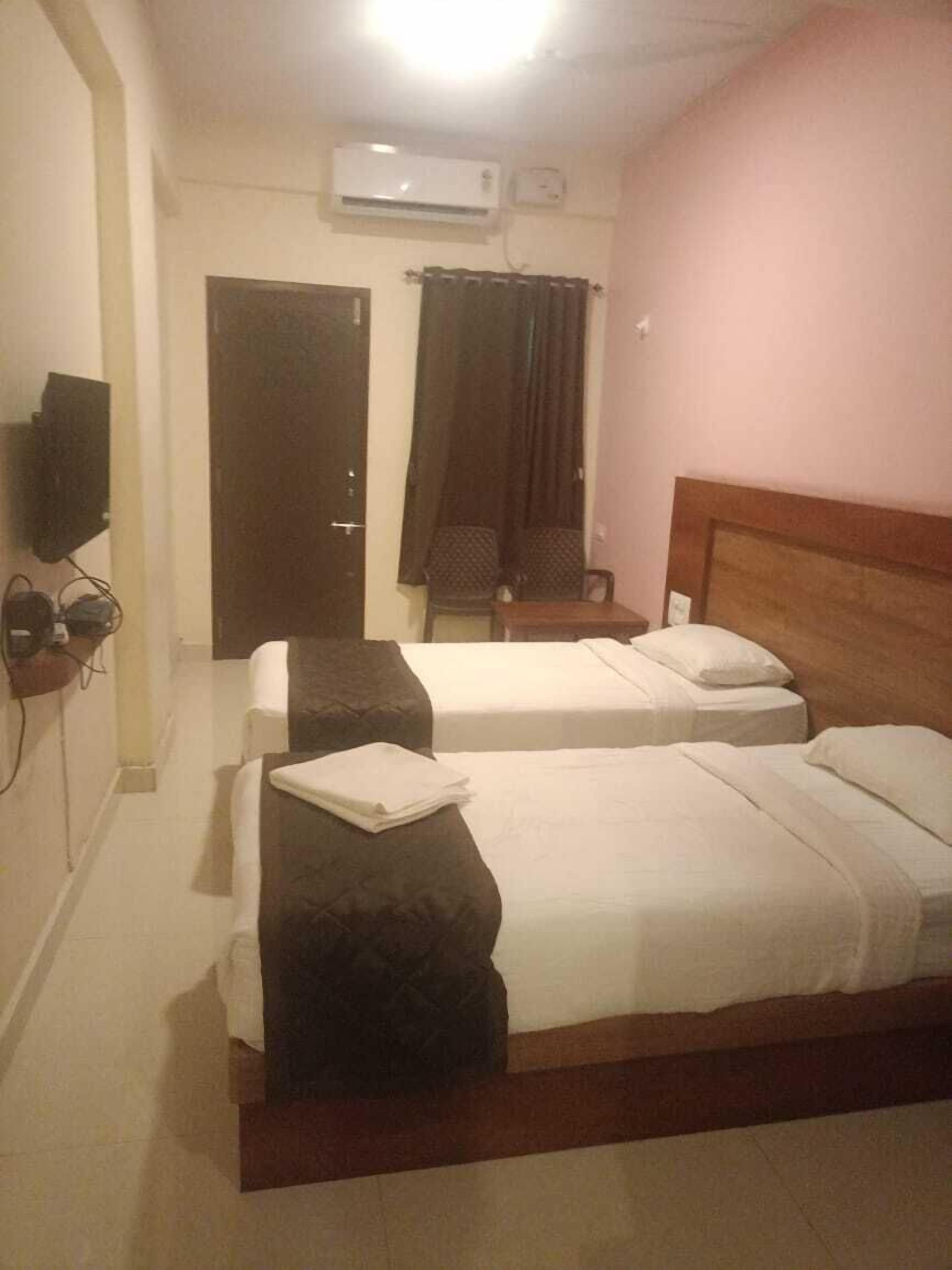 A hotel room with two beds, a TV, an air conditioner, and a door.
