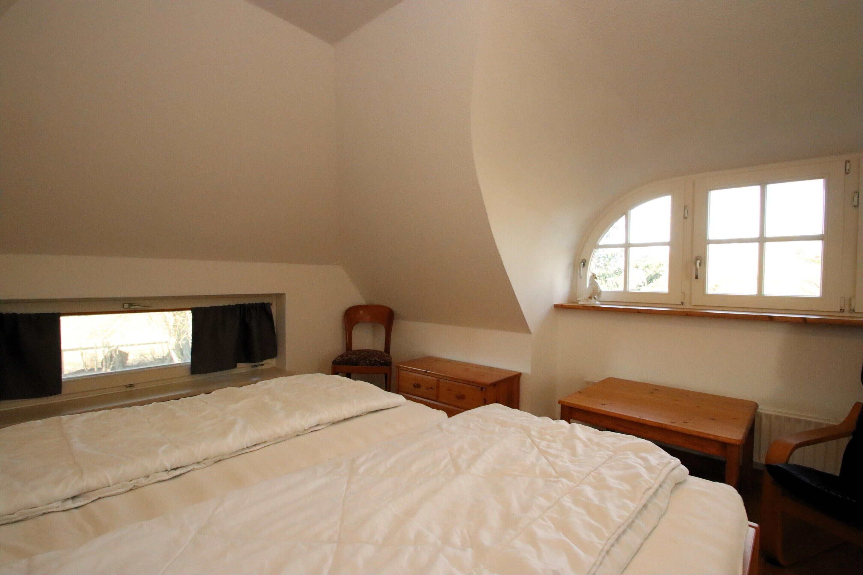 A bedroom with a single bed, a wooden desk, a chair, a window with curtains, and a cabinet.