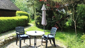 A patio with a round table and two chairs, an umbrella, and a brick wall. - Ferienwohnung im Reetdachhaus, Burhave (Butjadingen)