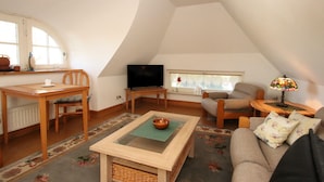 A cozy attic living space with a dining area, a television, a sofa, and a lamp. - Ferienwohnung im Reetdachhaus, Burhave (Butjadingen)
