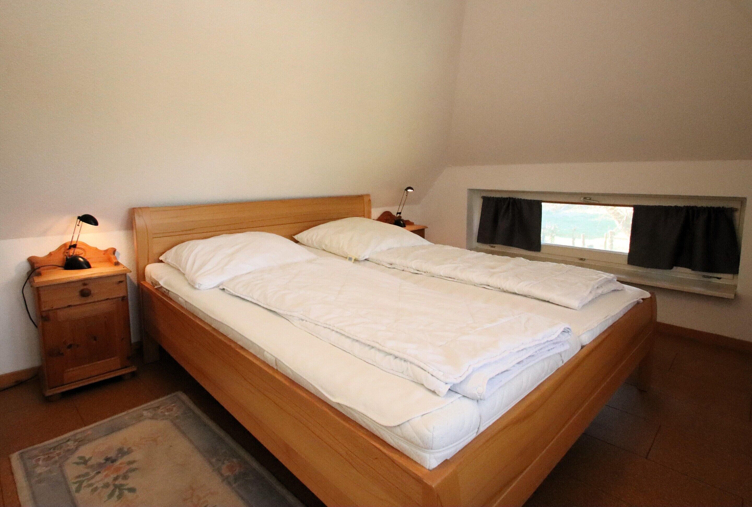 A single bed with a wooden headboard, a bedside table with a lamp, and a window with curtains.