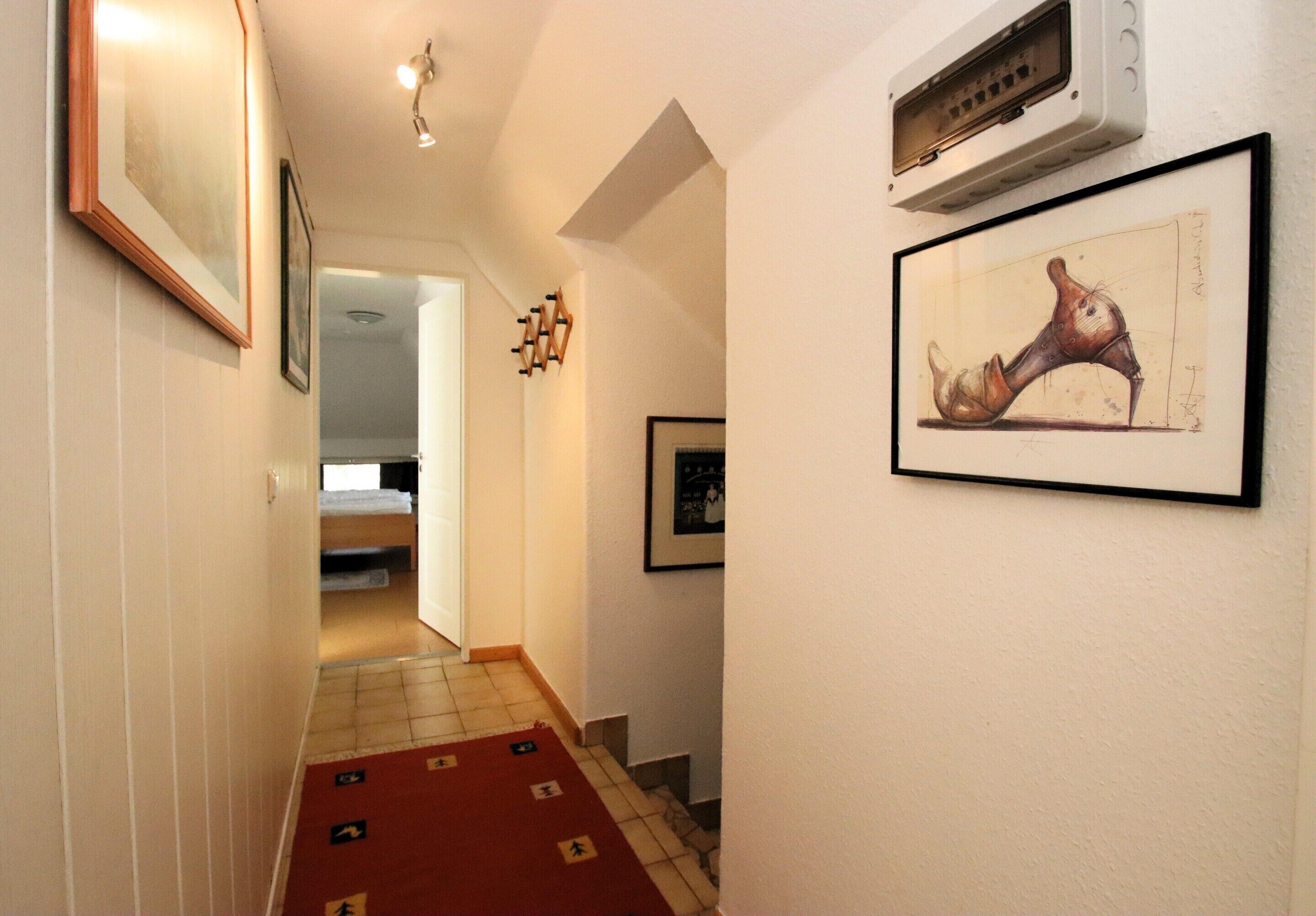 A hallway with a red carpet, framed artwork, and a ceiling light fixture.