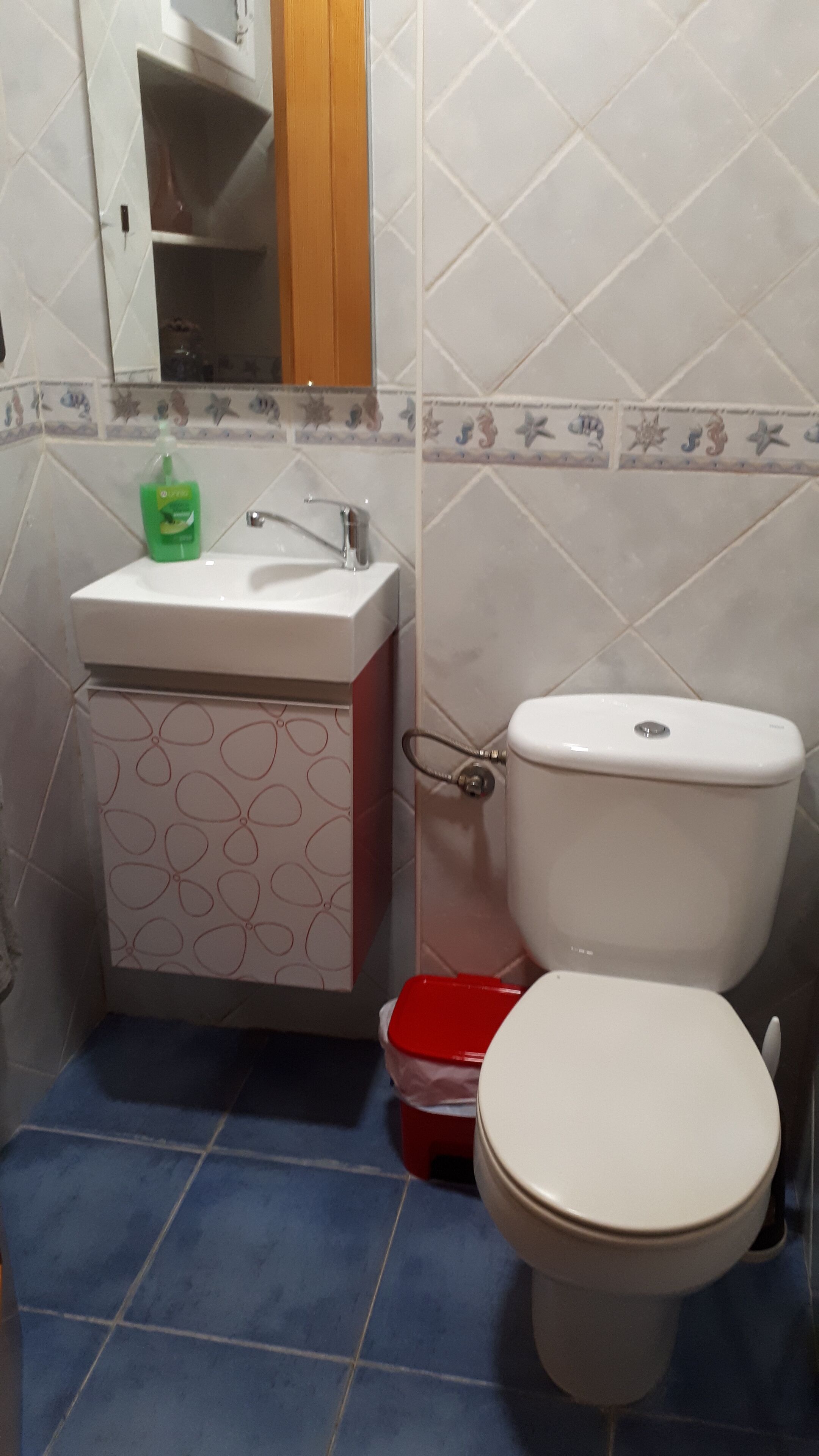 Un baño con inodoro, lavamanos y un cubo de basura rojo.