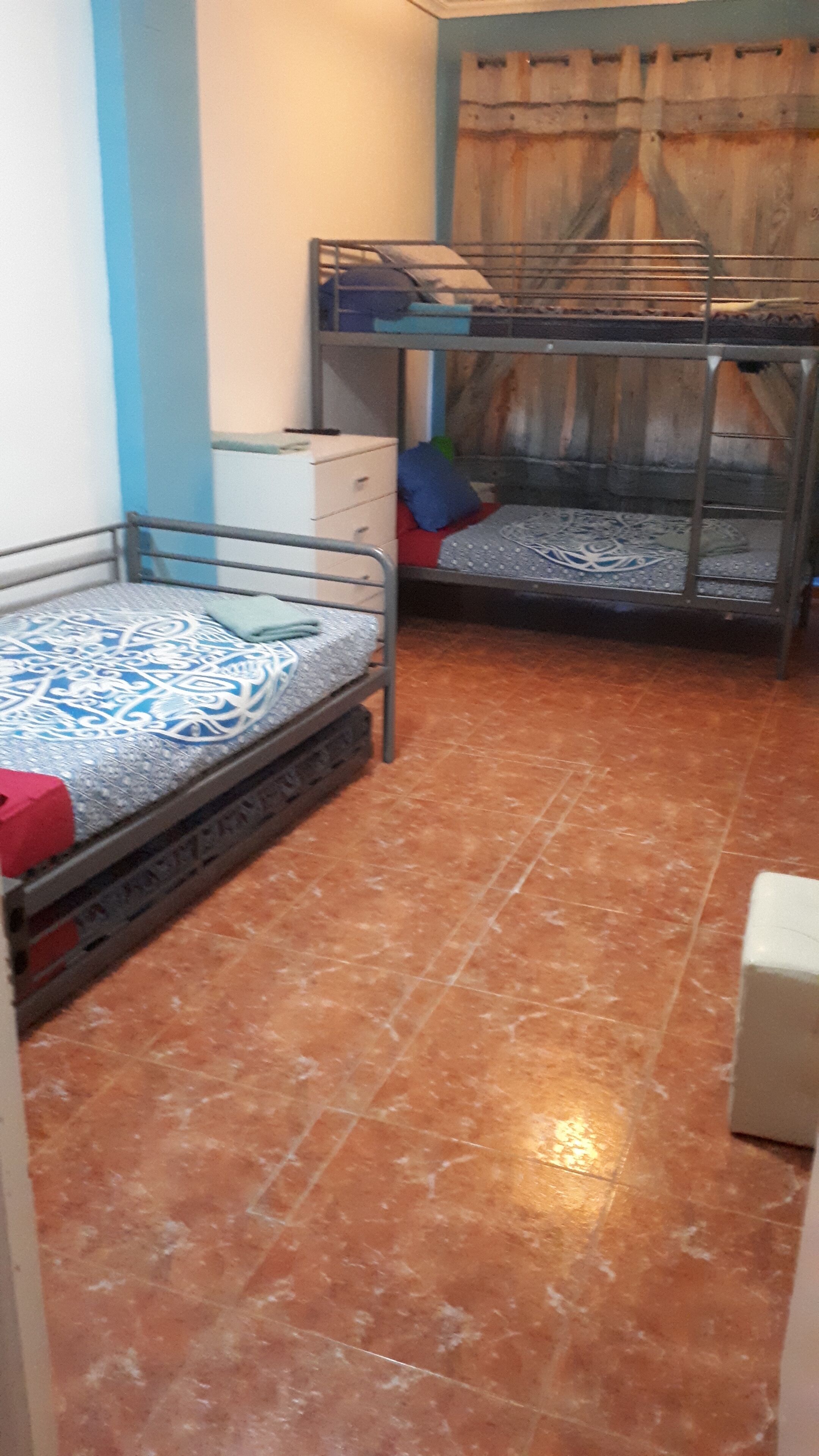 A dormitory room with bunk beds, a small dresser, and a tiled floor.