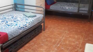 A dormitory room with bunk beds, a small dresser, and a tiled floor.