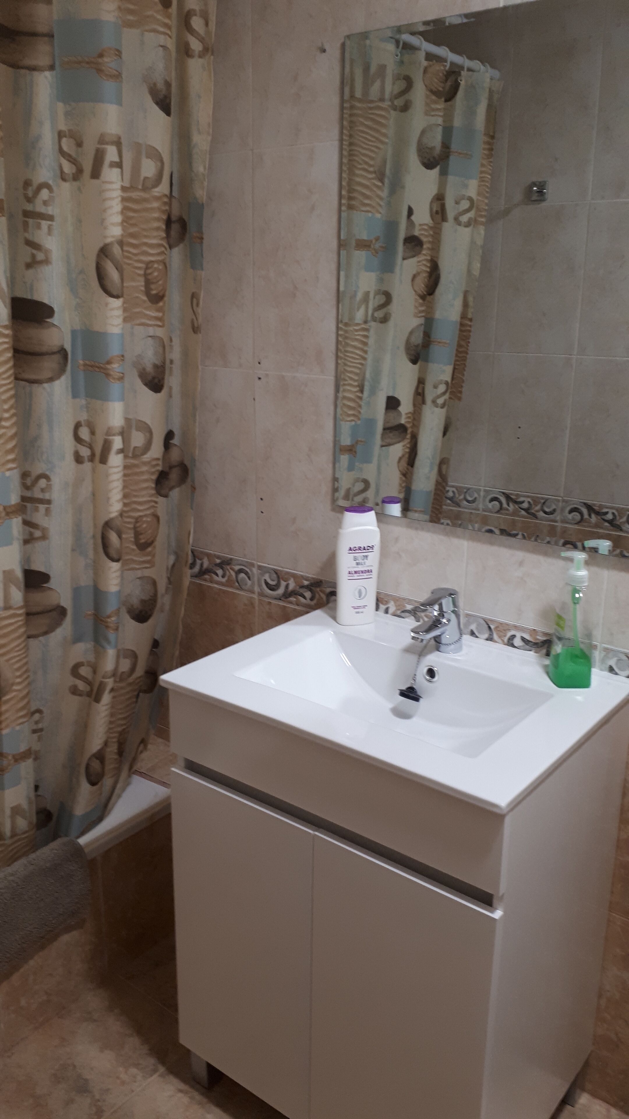 Een badkamer met een witte wastafel, een spiegel en een douchegordijn met een patroon.