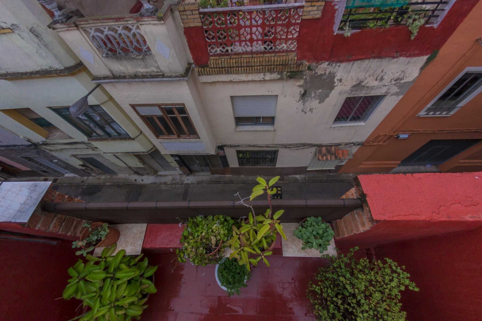 A narrow alleyway between buildings with balconies, potted plants, and a red awning.