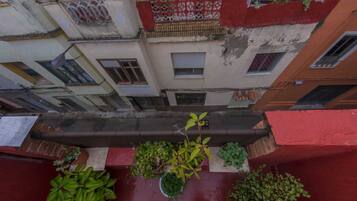 A narrow alleyway between buildings with balconies, potted plants, and a red awning.