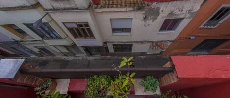 A narrow alleyway between buildings with balconies, potted plants, and a red awning.