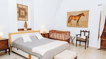 A bedroom with a bed, a chair, a rug, a painting, and a small table with a lamp.