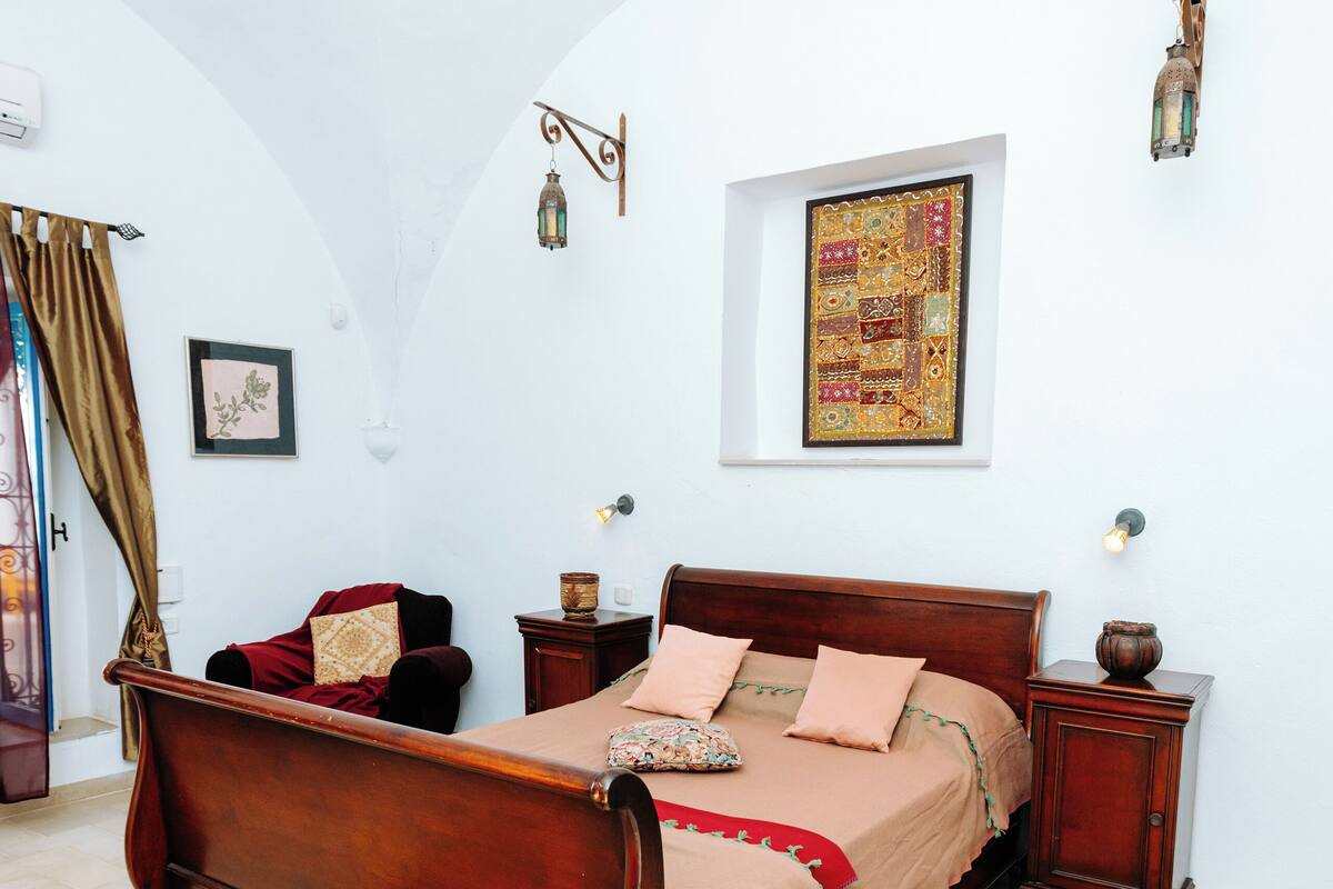 Une chambre à coucher avec un lit en bois, une table de chevet, une lampe fixée au mur et un tableau encadré.