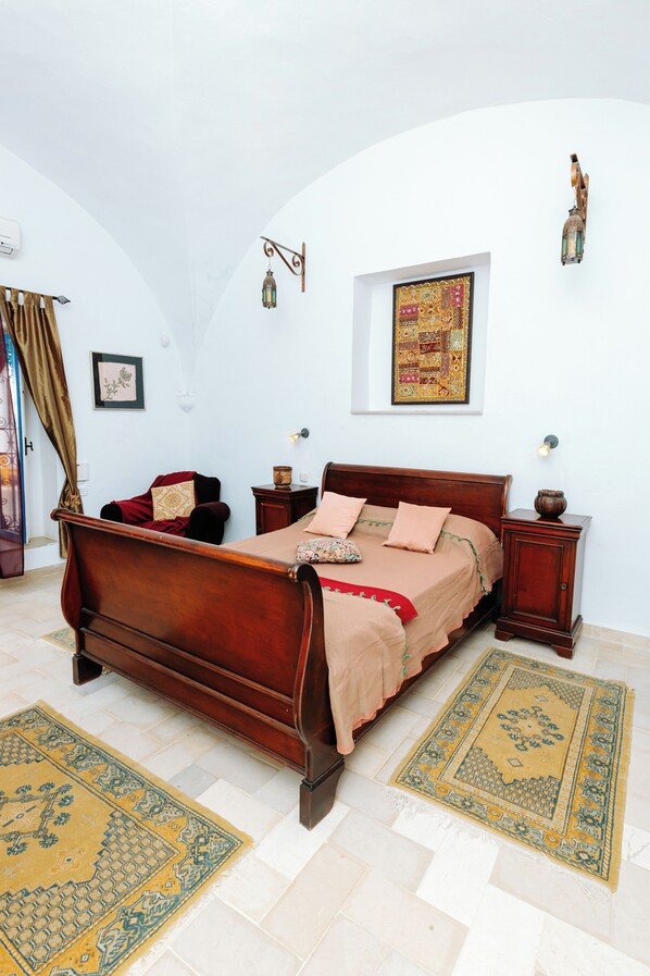 A bedroom with a wooden bed, a nightstand, a wall-mounted lamp, and a framed picture.