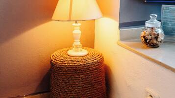 A lamp on a woven stool, a textured rug, and a small jar on a ledge.