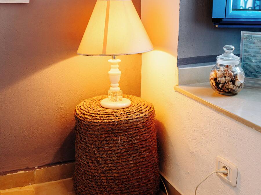 A lamp on a woven stool, a textured rug, and a small jar on a ledge.