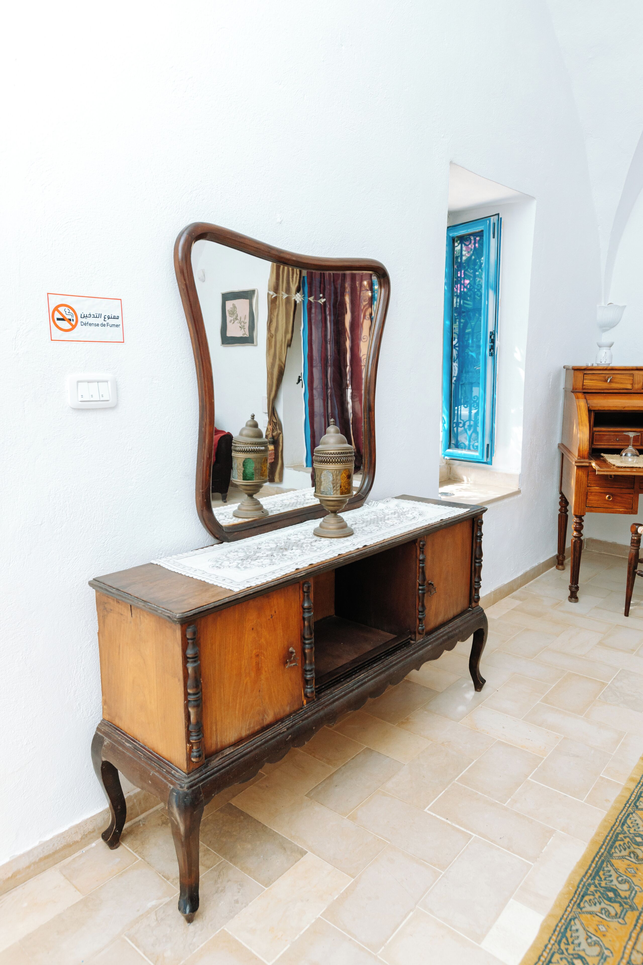 A vintage wooden dresser with a mirror, a small table, and a blue door in the background.