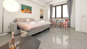 Et moderne hotelværelse med en seng, et skrivebord og en stol. Der er et billede på væggen, et vindue med gardiner og en lampe.