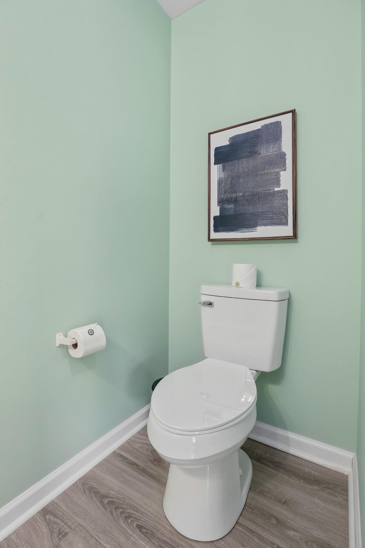 Un baño con inodoro, un rollo de papel higiénico y un cuadro abstracto enmarcado en la pared.