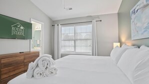 Habitación de hotel con cama, cómoda de madera, televisor de pantalla plana y ventana con persianas.