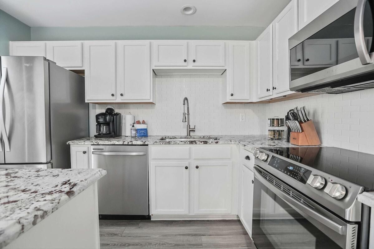 A modern kitchen with white cabinets, a stainless steel refrigerator, a dishwasher, a microwave, and an oven.