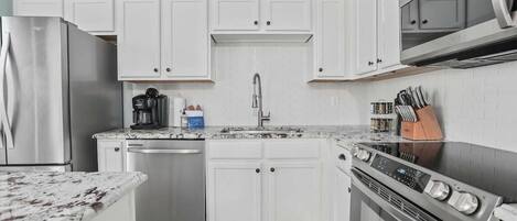 A modern kitchen with white cabinets, a stainless steel refrigerator, a dishwasher, a microwave, and an oven.